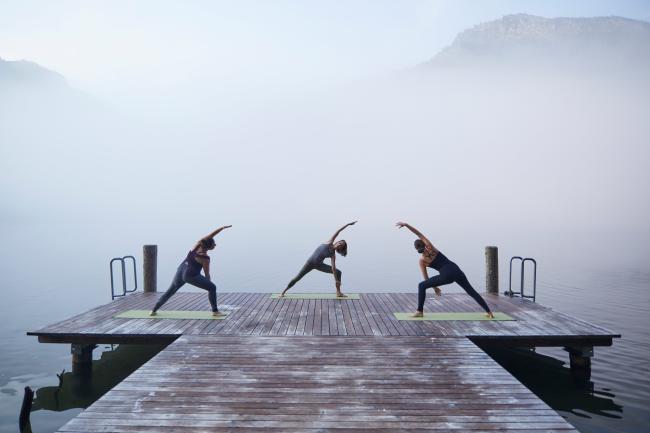 Drei Frauen, die auf einem Steg auf einem See im Nebel Yoga machen